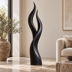 Può includere: Una scultura alta da pavimento realizzata in legno tinto di nero scuro. L'oggetto presenta due forme verticali allungate simili a fiamme che si curvano verso l'alto da una base singola, mostrando una venatura del legno visibile sulla superficie.