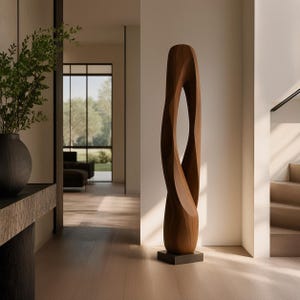 Può includere: Una scultura alta da terra realizzata in legno liscio color marrone medio. L'oggetto presenta una forma organica allungata e attorcigliata con un'apertura verticale centrale, montata su una base quadrata scura e semplice.