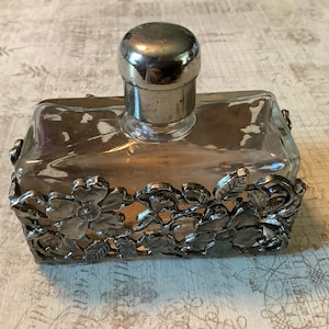 May include: A vintage glass perfume bottle with a silver stopper and a decorative silver floral design around the base.