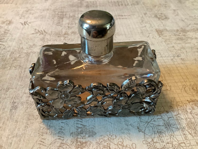 May include: A vintage glass perfume bottle with a silver stopper and a decorative silver floral design around the base.