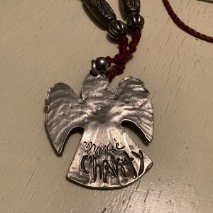 May include: A silver angel pendant necklace with the words "Marie Charity" inscribed on the pendant. The necklace has a red cord and silver beads.