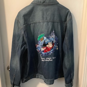 May include: A blue denim jacket with a colorful embroidered design on the back featuring Mickey Mouse in a wizard hat, a castle, and the text "Where magic lives Walt Disney World."