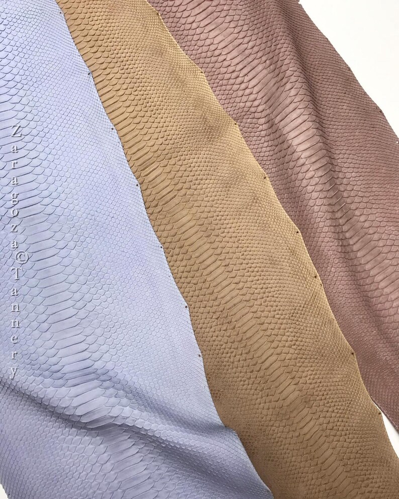 May include: Three strips of textured snake skin leather in light blue, tan, and dusty rose. The material features a repeating scale pattern throughout. The text "Zaragoza Tannery" is printed vertically along the left edge of the blue leather.