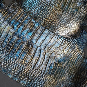 Puede incluir: Una pieza de cuero con un patrón texturizado y en relieve que imita la apariencia de la piel de cocodrilo. La superficie muestra un acabado metálico con un degradado de negro profundo, azul brillante y sutiles reflejos dorados en las escamas.