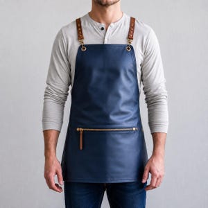 Op de afbeelding: Een marineblauw schort met een gladde, matte afwerking en een horizontale zak met ritssluiting aan de voorzijde. Het schort wordt vastgemaakt met bruine leren riemen die zijn bevestigd met goudkleurige metalen hardware, klinknagels en karabijnhaken.