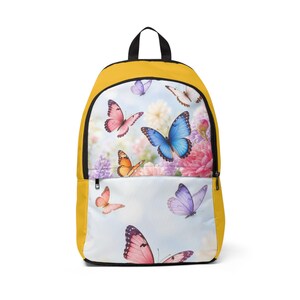 Puede incluir: Una mochila de color amarillo mostaza con un panel frontal estampado con una vibrante escena de jardín llena de varias mariposas coloridas en tonos azul, rosa, naranja y morado, sobre un fondo suave de flores en floración.