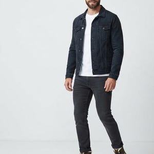 Könnte beinhalten: Eine dunkelgraue Jeansjacke über einem schlichten weißen T-Shirt, kombiniert mit einer passenden dunkelgrauen Jeans und schwarzen Schnürstiefeln mit buntem, abstraktem Muster an den Seiten und einem hellen Kunstfellfutter.