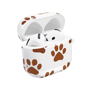 Puede incluir: Una funda protectora blanca para auriculares inalámbricos con un patrón repetitivo de huellas de patas marrones. La funda está abierta, revelando dos auriculares inalámbricos blancos con detalles negros en el compartimento de carga.