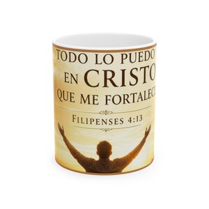 Puede incluir: Una taza de cerámica blanca con un fondo de atardecer dorado y la silueta de una persona con los brazos levantados. El texto dice: TODO LO PUEDO EN CRISTO QUE ME FORTALECE FILIPENSES 4:13 en letras de color marrón oscuro con adornos.