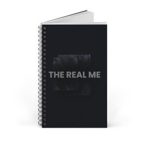 Puede incluir: Un cuaderno de espiral negro con un gráfico cuadrado oscuro y texturizado en el centro. El texto THE REAL ME está impreso en letras mayúsculas de color gris claro y en negrita en el medio de la portada. El cuaderno está ligeramente abierto arriba.