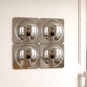 Puede incluir: Un conjunto de cuatro espejos de pared cuadrados dispuestos en una cuadrícula de dos por dos. Cada espejo presenta un marco de tono plateado pulido con un centro convexo circular prominente que refleja la habitación en gran angular.