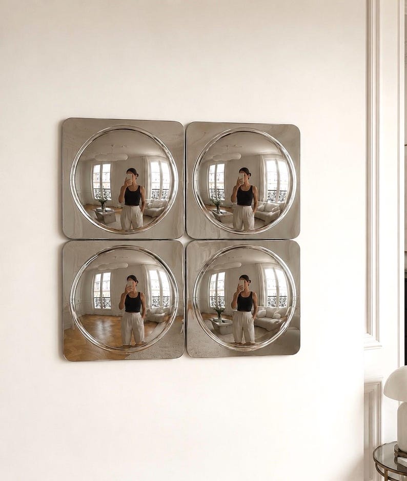 May include: A set of four square wall mirrors arranged in a two-by-two grid. Each mirror features a polished silver frame with a circular, convex centre that creates a wide-angle reflection of the room, including windows and furniture.