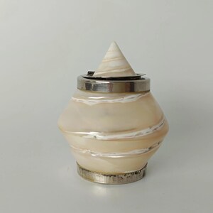 May include: A small, rounded container with a pearlescent, cream-colored body featuring swirling white bands. It has a metallic silver base and a matching silver rim, topped with a removable, conical lid that matches the body's marbled texture.