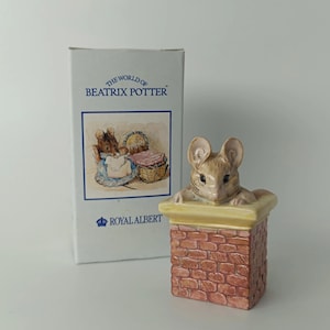 Op de afbeelding: Een keramieken beeldje van een bruine muis die uit een rechthoekige bakstenen schoorsteen kijkt, vergezeld van de originele witte kartonnen doos met de tekst The World of Beatrix Potter en het Royal Albert logo in blauwe inkt.