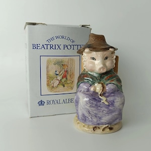 Peut inclure: Une figurine en céramique représentant un cochon portant un chapeau marron, un châle vert et une robe violette, tenant un petit objet. À côté se trouve une boîte en carton blanche marquée THE WORLD OF BEATRIX POTTER et ROYAL ALBERT.