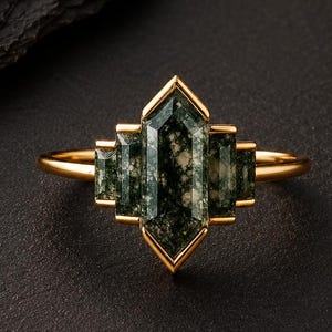 Pode incluir: Um anel de ouro com uma pedra central de ágata musgosa hexagonal alongada, ladeada por duas pedras retangulares menores de cada lado. As pedras estão cravadas numa armação de ouro com um aro fino e polido.
