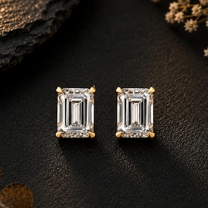 May include: A pair of stud earrings featuring emerald-cut clear gemstones set in yellow gold prongs. Each rectangular stone displays a faceted surface with vertical lines, held securely by four small gold corner claws, creating a classic and symmetrical jewellery design.