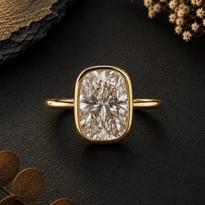 May include: A gold ring featuring a large, rectangular cushion-cut gemstone with rounded corners, set in a smooth, polished gold bezel setting. The band is thin and circular, crafted from the same yellow gold metal as the central setting.