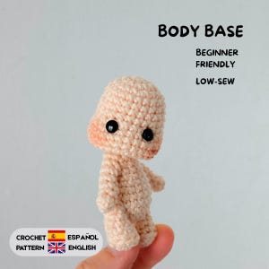 Op de afbeelding: Een licht perzikkleurige gehaakte poppenlichaambasis met twee kleine zwarte plastic ogen. De tekst op de afbeelding luidt: BODY BASE, BEGINNER FRIENDLY, LOW-SEW, CROCHET PATTERN, ESPAÑOL, ENGLISH. De pop heeft een afgerond hoofd en een klein lijfje.