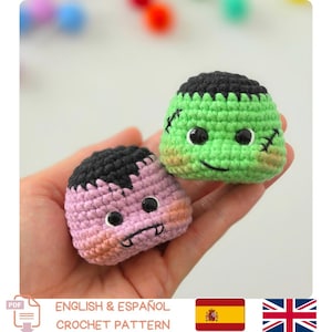 Puede incluir: Dos pequeños juguetes de peluche tejidos a ganchillo, de forma redonda. Uno es verde claro con cabello negro, ojos negros y cicatrices bordadas. El otro es morado claro con cabello negro, ojos negros y dos pequeños colmillos blancos.
