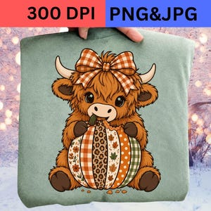 Może przedstawiać: Bluza w kolorze szałwiowej zieleni z grafiką puszystej brązowej krowy rasy highland z dużą pomarańczowo-białą kokardą w kratkę na głowie. Krowa trzyma dynię ozdobioną pionowymi pasami w kratkę, wzór w panterkę oraz motywy liści.