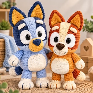 May include: Two crochet plush toys representing cartoon dogs. The left figure is blue with dark blue ears and a cream belly. The right figure is orange with dark orange ears and a cream belly. Both have large black eyes and stitched smiles.