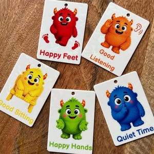 May include: Five rectangular white plastic cards featuring colorful cartoon monsters. The cards display the text Happy Feet, Good Listening, Good Sitting, Happy Hands, and Quiet Time, each accompanied by a corresponding monster illustration.