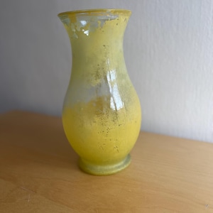 Op de afbeelding: Een gele glazen vaas met een matte, getextureerde afwerking. De vaas heeft een bolvormig lichaam dat taps toeloopt naar een smalle hals en licht uitloopt bij de rand. De gele kleur is geconcentreerder aan de basis en vervaagt naar de bovenkant.