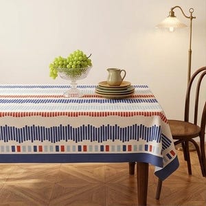 Peut inclure: Une nappe rectangulaire présentant un motif géométrique de barres verticales bleues, bleu clair et rouges sur un fond crème. Le design comprend des bandes horizontales de longueurs variées et une bordure bleu foncé unie sur les bords.
