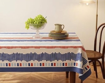 May include: A rectangular tablecloth featuring a geometric pattern of vertical blue, light blue, and red bars on a cream background. The design includes horizontal bands of varying stripe lengths and a solid dark blue border along the edges.