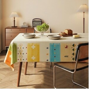 Peut inclure: Une nappe rectangulaire dotée d'une base couleur crème avec des panneaux verticaux verts, orange, jaunes et bleus. Le tissu est orné de petits motifs géométriques, notamment des croix, des losanges et des silhouettes d'animaux stylisées.