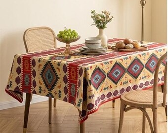 Op de afbeelding: Een rechthoekig tafelkleed met een herhalend geometrisch patroon in tinten rood, blauw en donkerbruin op een crèmekleurige achtergrond. Het ontwerp bevat ruitvormen en verticale strepen die het oppervlak van een houten tafel bedekken.