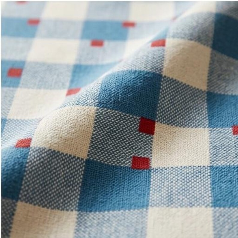 May include: A woven fabric featuring a blue and off-white checkered pattern with small, solid red squares positioned at the intersections of the grid lines. The textile has a visible, textured weave and is draped to show depth and folds.