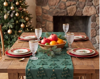 Op de afbeelding: Een donkergroene tafelloper met een textuur van kerstbomen en gouden sterren, geplaatst op een houten tafel met rood-witte kerstborden, helder glaswerk met textuur, goudkleurig bestek en een gevlochten schaal met vers fruit.
