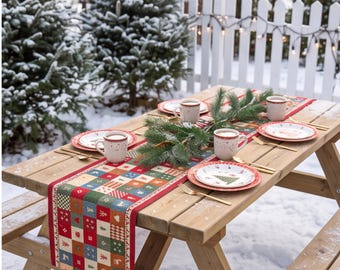 Op de afbeelding: Een houten picknicktafel gedekt voor vier personen met een rood, groen en wit geblokte tafelloper met kerstmotieven. De set bevat witte keramische borden met boompatronen, bijpassende mokken en goudkleurige metalen vorken.