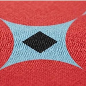 May include: A woven fabric featuring a repeating geometric pattern of large red circles on a light blue background, with a small black diamond shape centered in the negative space created between the intersecting circular forms.