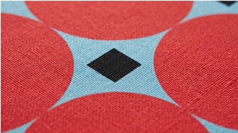 May include: A woven fabric featuring a repeating geometric pattern of large red circles on a light blue background, with a small black diamond shape centered in the negative space created between the intersecting circular forms.