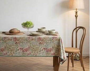 Puede incluir: Un mantel rectangular con un denso estampado floral en tonos rosa, verde y crema con un borde festoneado de color verde oscuro. La mesa está dispuesta con una tabla de cortar de madera con una hogaza de pan, un cuenco de cristal con uvas verdes y cuencos de cerámica apilados.
