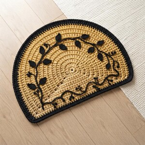 May include: A semi-circular crochet rug featuring a mustard yellow base with a thick black border. The center is decorated with a black crocheted vine pattern that includes small leaves and stems, creating a detailed botanical design.