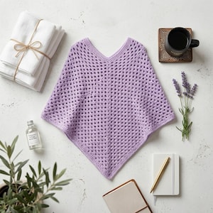 May include: A light purple crochet poncho featuring a V-neckline and a repeating diamond-shaped openwork pattern. The garment is crafted from yarn and displays a pointed hemline, showcasing a consistent texture throughout the entire piece.