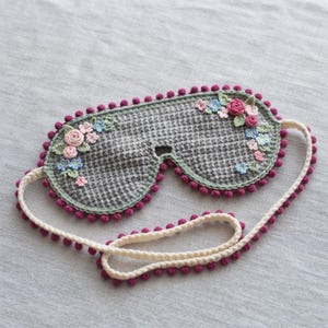 Gehaakt slaapmasker met bloemenmotief (PDF-patroon), oogmasker met zeggesteek en mini-bloemen, magenta pomponrand en verstelbare crèmekleurige band.