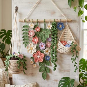 May include: A crochet wall hanging featuring a wooden dowel with various hanging flowers, green leaves, and vines, alongside a matching crochet hanging planter with trailing greenery and a triangular crochet wall pocket containing small flowers.