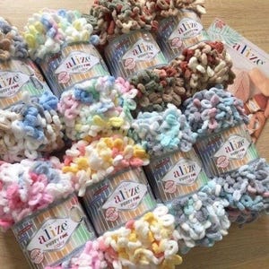 May include: A collection of Alize Puffy Fine Color yarn skeins in various pastel and earth-toned variegated loops. Each skein features a white paper label with the Alize brand logo and the text Puffy Fine Color. The yarn has a soft, looped texture.