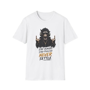 May include: A white short-sleeve t-shirt featuring a graphic of a chimpanzee wearing sunglasses and headphones, making a rock-and-roll hand gesture. Below the graphic, the text reads: STAY HUNGRY STAY FOOLISH NEVER SETTLE in black and gold.