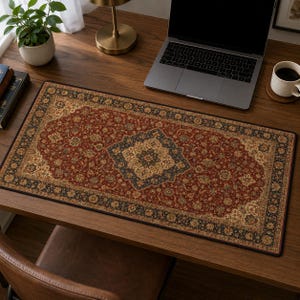 May include: A rectangular desk mat featuring a detailed, intricate pattern in shades of deep red, black, and cream. The design mimics a traditional woven rug with a central medallion, floral motifs, and a decorative border, providing a flat surface.