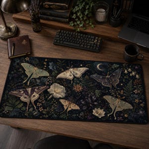 May include: A rectangular desk mat featuring a dark botanical print with various moths, including pale green and brown species, interspersed among white flowers, ferns, and foliage against a deep navy background with a crescent moon.