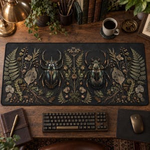 May include: A rectangular desk mat featuring a dark background with two large, detailed beetles centred among various botanical elements, including ferns, dried leaves, and small berries, arranged in a symmetrical, nature-inspired pattern.