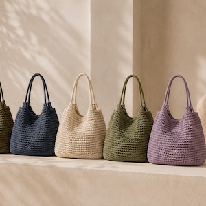 May include: Six hobo-style tote bags arranged in a row, each featuring a textured, woven crochet construction with two shoulder straps. The bags are presented in a variety of solid colors including black, olive green, navy blue, cream, sage green, and lavender.