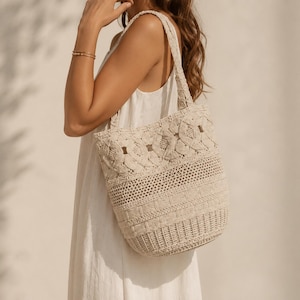 May include: A beige crochet tote bag featuring a complex knotted pattern at the top, followed by a section of open mesh stitching, and a base with a dense, textured woven design. The bag includes two matching shoulder straps made of crochet.