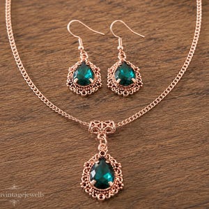 Puede incluir: Un conjunto de collar y pendientes en oro rosa con cristales verde esmeralda en forma de l&aacute;grima. El colgante y los pendientes est&aacute;n enmarcados por un intrincado trabajo de filigrana met&aacute;lica. El collar incluye una cadena fina y ganchos.